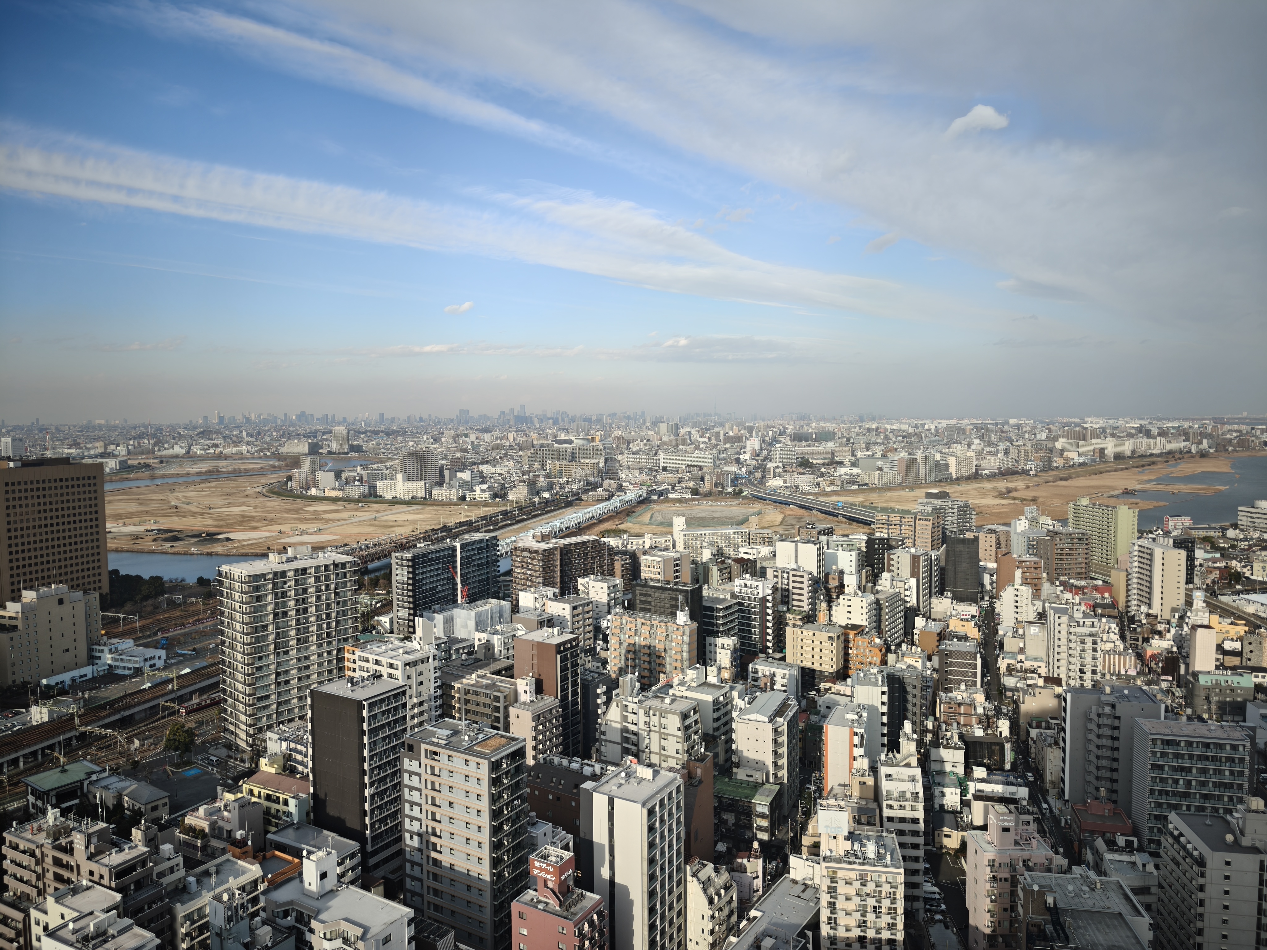 多摩川铁路桥和延伸到远方东京市区的铁路线，放大仔细看还隐约可见东京塔、晴空塔和彩虹桥